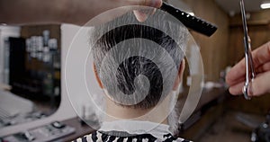 Close-up back view of hands with scissors and comb cutting gray hair in barber shop