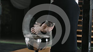 Close-up back view male weight lifter athlete applying talc powder before exercising in large hardcore gym hall.