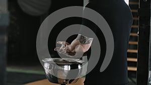 Close-up back view male weight lifter athlete applying talc powder before exercising in large hardcore gym hall.