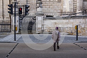 Close up back view of man crossing street. Red light on semaphore, danger.