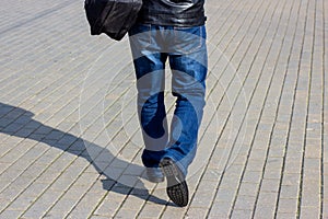 Close up back view of a pedestrian man in the jeans with the bag walking in the street.