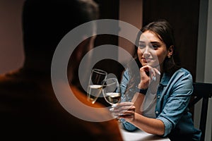 Close-up back view to smiling pretty young woman talking celebration toast and clinking white wine glass with husband