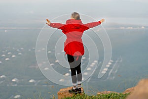 Close up back of woman wear red coat and stand with spread her arms near cliff on the mountain and look forward to beautiful view