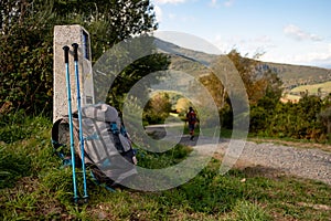 Close up of backpack with walking stick and Camino de Santiago sign, with pilgrim walking along the path, symbol of pilgrimage and