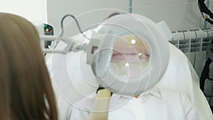 Close up backside view cosmetologist examines area around lips of patient through cosmetic magnifying glass