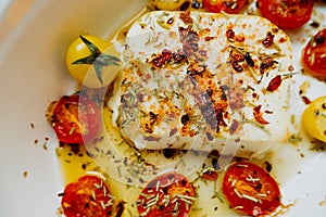 Close-up baked molten feta cheese with small tomatoes in olive oil with herbs and spices. simple cheese dishes. vegan menu,