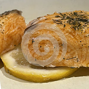 Close up of baked Salmon with lemon and herbs on white plate background