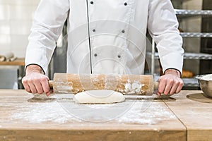 close up of baker hands rolling out raw dough