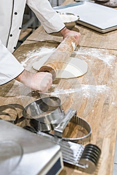 close up of baker hands rolling out uncooked dough