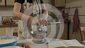 Close-up of bakery concept - Woman sift cocoa powder through metallic sieve to glass bowl