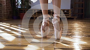 Close-up of ballerina graceful feet in ballet shoes dancing ballet elements on wood floor at ballet class. Dancing