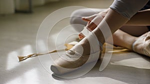 Close-up of ballerina`s feet. Ballerina preparing for training, and tying ribbon of pointe shoes sitting on floor in