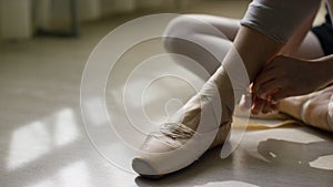 Close-up of ballerina`s feet. Ballerina preparing for training, and tying ribbon of pointe shoes sitting on floor in