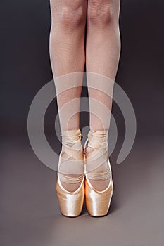 Close-up of Ballerine feet in pointe shoes on grey background. Ballerina is standing on the hips. Studio shot of ballerina legs in