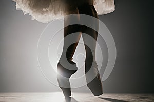Close up of ballet dancer as she practices exercises on dark stage or studio. Woman`s feet in pointe shoes. Ballerina