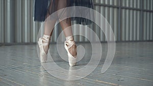 Close-up of ballet dancer`s legs in pointe shoes, tights and mesh skirt dancing on pointe in a choreography room. Ballet