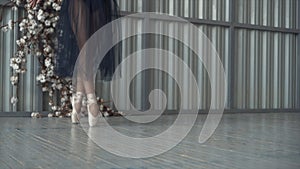 Close-up of ballet dancer`s legs in pointe shoes, tights and mesh skirt dancing on pointe in a choreography room. Ballet