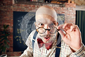 Close-up of balm man in glasses with moustaches looking at camera with attention. Scientist in classroom