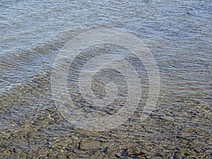 Close up of Baltic sea ripple on water surface with sunlight reflecting on a sunny day. Small smooth brown stones