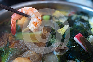 Close up bamboo chopsticks holding shrimp on Double flavor hot pot with meat seafood medicinal herbs vegetables