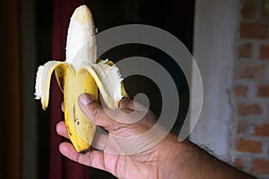 Close up of a banana peeled banana against a dark brick wall background