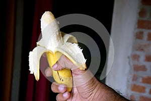Close up of a banana peeled banana against a dark brick wall background
