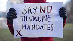 Close-up banner Say no to vaccine mandates in female hands outdoors. Unrecognizable woman posing with anti vax placard