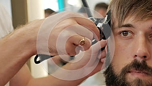 Close-up barber trimming temples of a stylish bearded man with electric razor