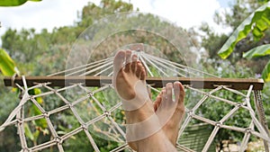 Close up of bare feet of a man resting in a hammock on a sunny day.