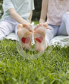 close-up on the bare feet of two children drawing red hearts. Cheerful childhood, childish love