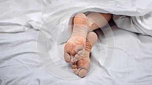 Close up bare female foot lying on comfortable bed under blanket. Shot on RED Raven 4k Cinema Camera