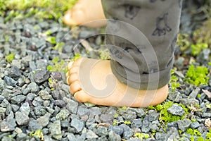 Close up of the bare foot of the child walking on over gravel and copy space