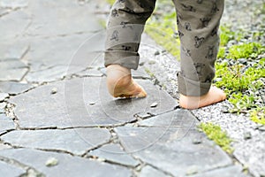 Close up of the bare foot of the child walking on stone pavement and copy space