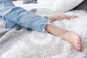 Close-up of barefoot attractive female legs dressed blue jeans in bed, home relaxation and rest