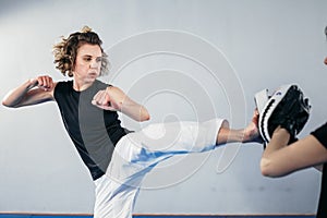 Close-up of barefoot woman leg practicing kicking with taekwondo coach who holds boxing paw. Concentrated active female kicking