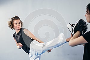 Close-up of barefoot woman leg practicing kicking with taekwondo coach who holds boxing paw. Concentrated active female kicking