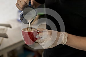 Close up barista pouring steamed milk into coffee cup making beautiful latte, cappuccino art Rosetta pattern. Close up barista