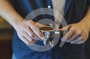 Close up, Barista presses holding espresso handle filled with ground coffee, prepares espresso in his coffee shop