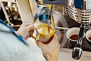 Close up of barista steaming milk in the pitcher with coffee machine.