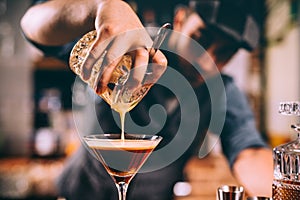 Close up of bartender hand pouring alcoholic cocktail in martini glass