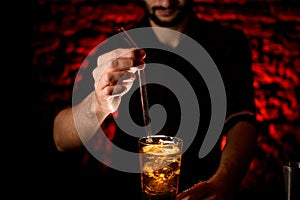 Close-up Barman`s hand adds glassy drinking tube to glass with cocktail.