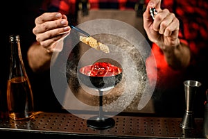 Close-up bartender decorates glass with large piece of ice and sprinkles on it