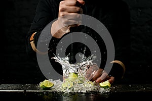 Close-up. Bartender holds madler and energetically squeeze slices of citrus to cocktail
