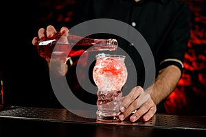 Close-up bartender pouring drink to glass full of pieces of ice.