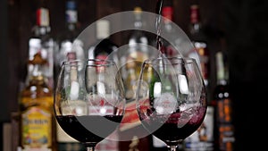 Close-up of a bartender pouring red wine into two glasses at a bar.