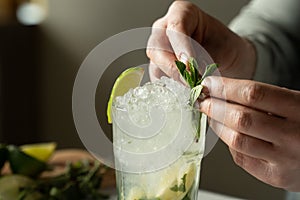 Close -up bartender prepares a mojito cocktail at the bar. A man decorates a Mojito cocktail with mint and lime