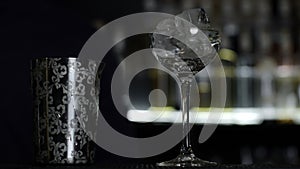 Close up of a bartender putting ice cubes into the small empty cocktail glass. Media. Details of making a drink with