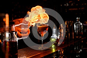 Close-up of bartender`s hands lighting a flame near glass with cocktail.