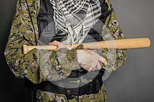 Close-up baseball bat in the hands of an unknown person in camouflage and body armor