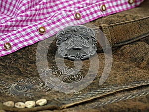 Close up bavarian lether belt with coat of arms on lederhose and pink check shirt, traditional clothing for Oktoberfest